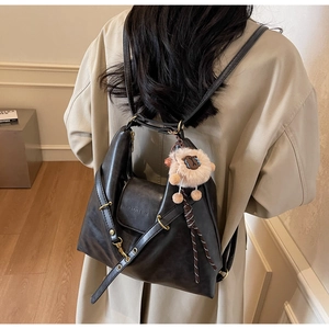 Macro detail of black matte leather tote bag with stylish white plush sheep pendant charm