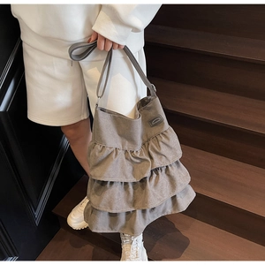 Nahaufnahme der grauen Canvas-Tasche mit Rüschen und Lederlogo auf einer Holztreppe
