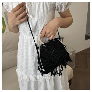 Detail of black woven rope bag featuring round wooden handles and bohemian tassel accents