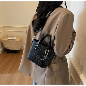 Détail d'un sac seau en cuir noir gaufré avec breloque chien sur une veste marron