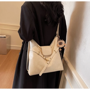 Detail view of a large cream tote bag with a sheep charm worn by a model in a black coat