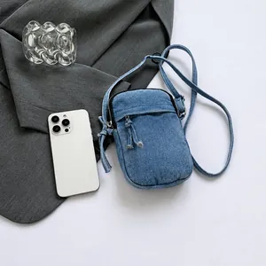 Detail view of blue washed denim crossbody phone bag with double zipper and pull cord