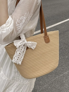 Woven straw tote bag with brown leather straps and large white lace bow in outdoor setting