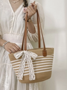 Large striped woven straw tote bag with brown leather handles and white lace bow