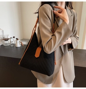 Detail of woven black shoulder bag with brown leather straps worn with a beige blazer