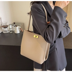 Detail of lychee textured leather bucket bag with gold lock worn by a model in a suit