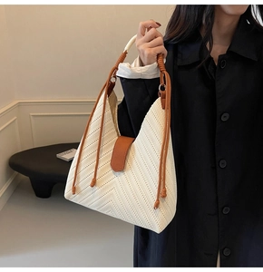 Detail view of woven herringbone knit texture and brown leather strap on cream tote bag