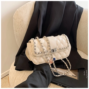Detail of quilted beige chain bag with classic silver twist lock and woven metal strap