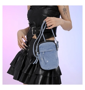 Macro detail of a washed denim mini crossbody bag with zipper and small pocket
