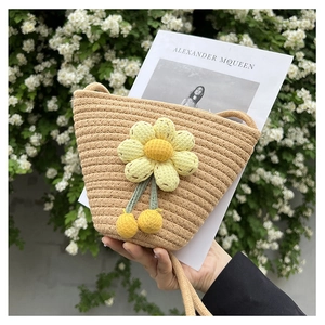 Close-up of woven straw bucket bag featuring a yellow sunflower and pompom detail