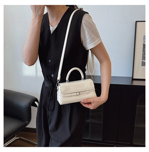 Close-up of a minimalist cream small square bag with top handle and thin shoulder strap