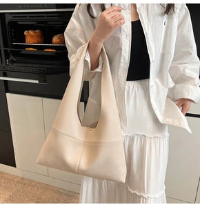 Minimalist beige lychee grain leather tote bag worn as a hobo shoulder bag for daily use
