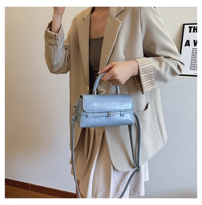 Detail of light blue patent leather handbag featuring a metal buckle and top handle