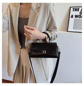 Detail of black glossy patent leather crossbody bag with silver hardware on model