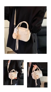 Close-up of cream Boston bag featuring bear charm, decorative ribbon and logo detail