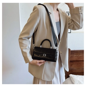 Detail showing a black glossy crossbody square bag worn over a beige suit jacket