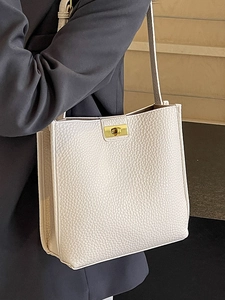 Minimalist beige litchi pattern bucket bag with golden lock on a grey suit blazer