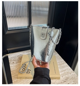 Silver metallic bucket bag with pleated texture and silver chain strap on marble