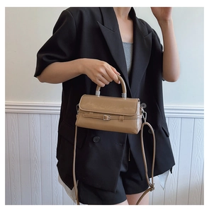 Detail of glossy khaki crossbody bag with top handle and thin strap on black suit