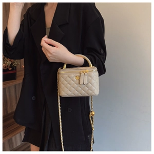Detail of beige quilted mini vanity bag featuring golden camellia charm and metal handle