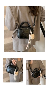 Detail view of glossy black pillow bag with embossed text and beige plush bear charm