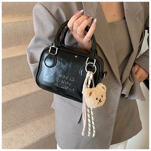 Detail of black glossy pillow bag with embossed text and plush bear charm decoration