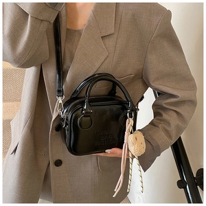 Detail of black patent leather bag featuring a logo stamp and cute plush bear charm