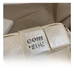 Close-up of the silver metal logo and premium woven leather texture of the beige square handbag