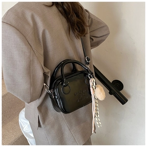 Polished black patent leather pillow bag with debossed lettering and plush charm detail
