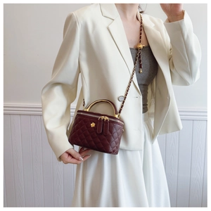 Model wearing a wine red quilted bucket bag with gold chain and handle in a sleek white outfit
