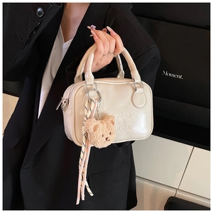 Close-up of beige minimalist pillow bag with plush bear and woven tassel accessories
