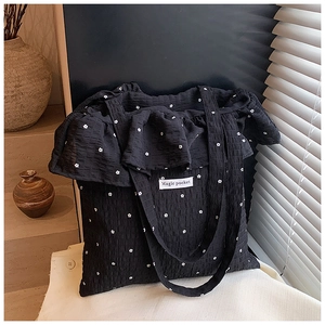 Detail of waffle textured black tote bag with white floral pattern and ruffle trim