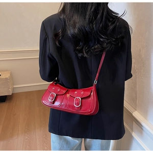 Close-up of red patent leather underarm bag featuring dual silver metal buckles detail