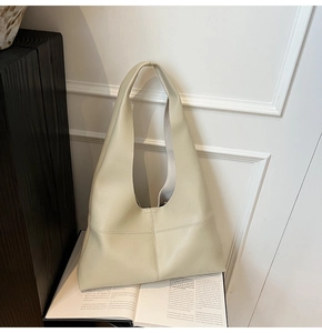 Close-up of a beige lychee grain leather hobo bag with stitched cross detail on base