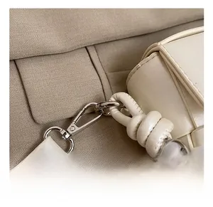 Detail of silver lobster clasp and decorative knots on a woven cream crossbody handbag