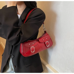 Detail view of a vintage red glossy patent leather underarm bag with silver buckles on a model