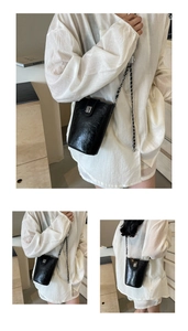 Detail of a black bucket bag with oil-wax texture and metal chain strap on white shirt