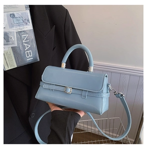 Close-up of light blue glossy patent leather handbag with silver buckle and hand-held detail