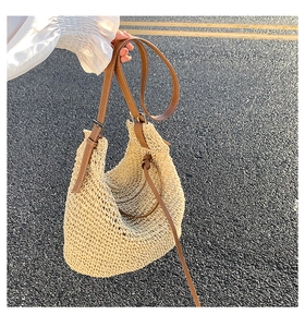 Detail of hand-woven straw tote bag featuring brown leather strap and drawstring closure