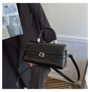 Detail of minimalist black handbag with silver buckle and glossy finish held by a model