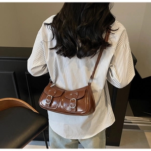 Detail view of brown glossy faux leather shoulder bag with double buckled pockets