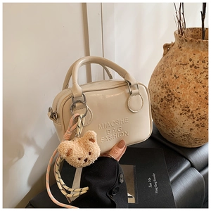 Close-up of cream faux leather pillow bag featuring embossed text and a cute bear charm