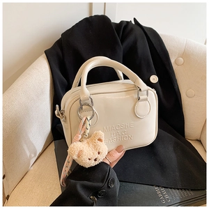 Close-up of creamy white PU leather pillow bag with debossed logo and cute bear charm