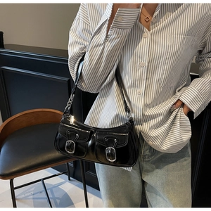 Close-up of black patent leather underarm bag featuring silver buckles and chain strap detail