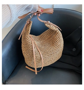 Detail view of woven straw shoulder bag featuring adjustable brown leather strap and buckle