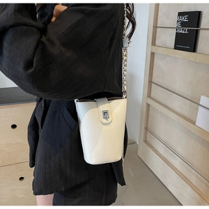 Close-up of a white leather bucket bag with silver metal clasp and chain strap detail