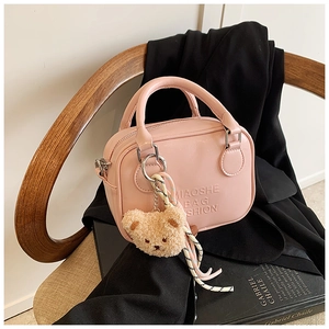 Pink PU leather handbag with bear charm and ribbon on a chair with a blazer