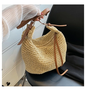Detail of beige woven straw tote bag with brown leather strap and metal buckle closure