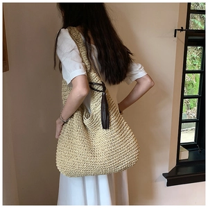 Close-up of woven straw tote bag featuring intricate hollow patterns and brown tassel detail