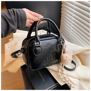 Black leather pillow bag with dual handles and pink plush bear charm detail